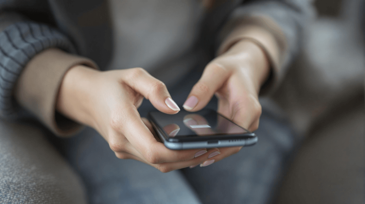 ソファに座りスマートフォンをスワイプ操作する女性の手元イメージ