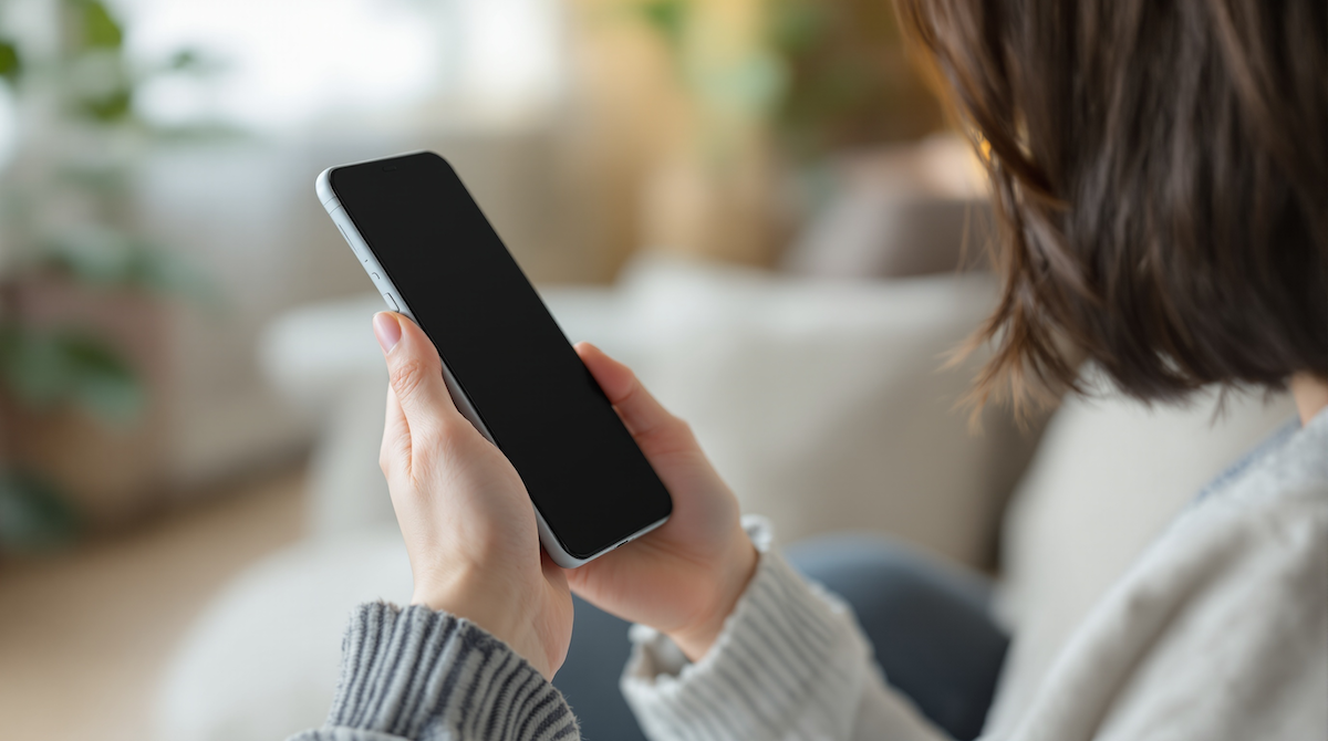女性が室内でスマートフォンを両手に持ち、横から見た構図